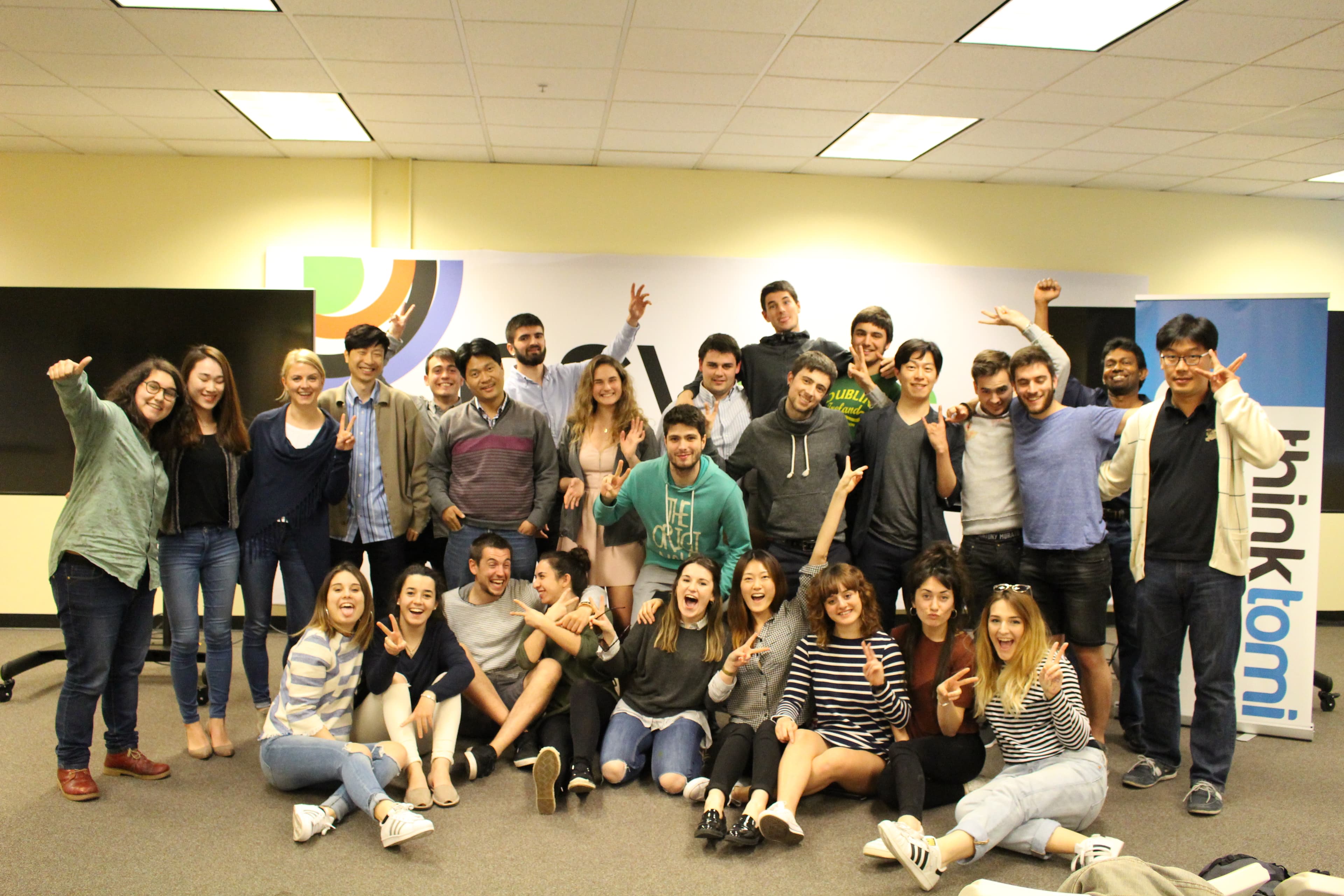 A European programme cohort gathered together in a classroom beside a thinktomi banner.